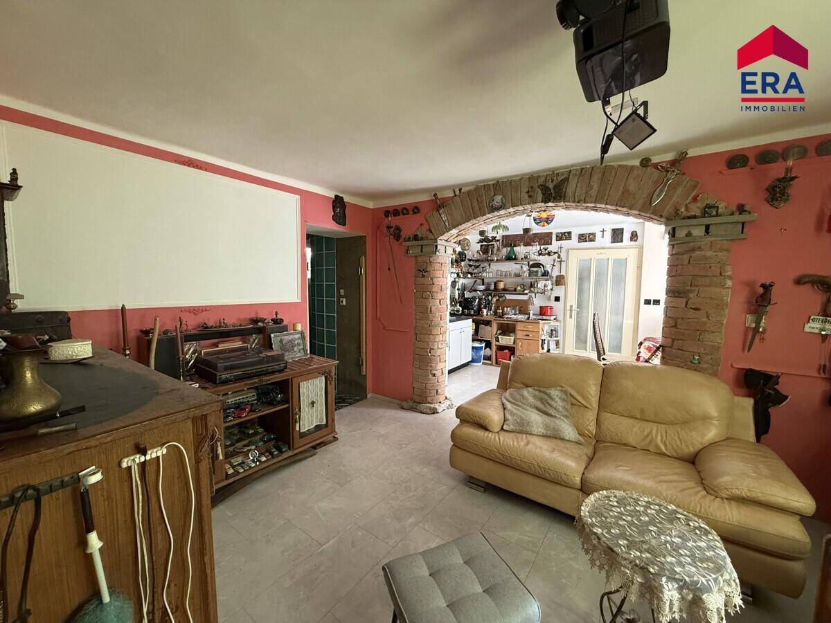 Wohnzimmer mit beigem Sofa, rustikalem Schrank und einem dekorativen Ziegelbogen zu einem weiteren Raum.