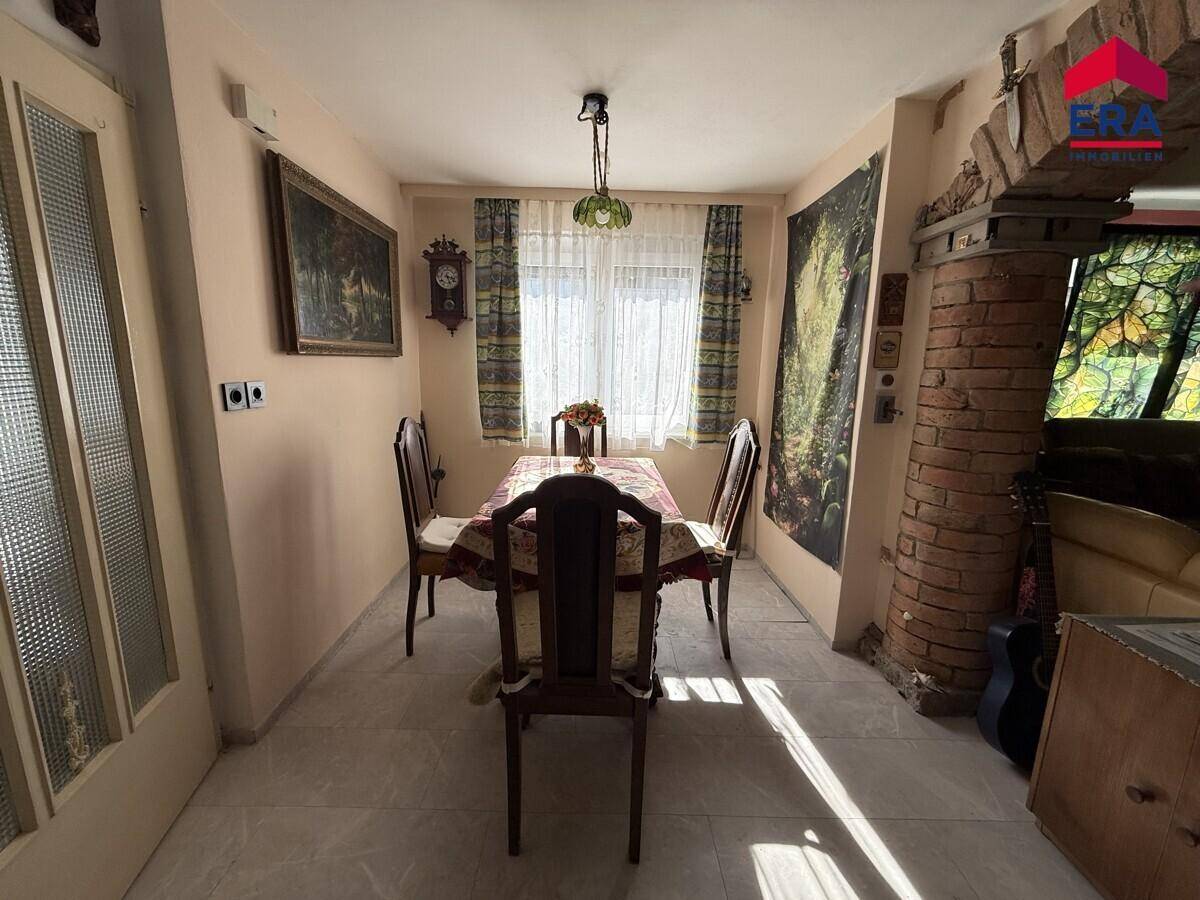 Essbereich mit einem traditionellen Holztisch, Stühlen und einem Fenster, das Tageslicht hereinlässt.