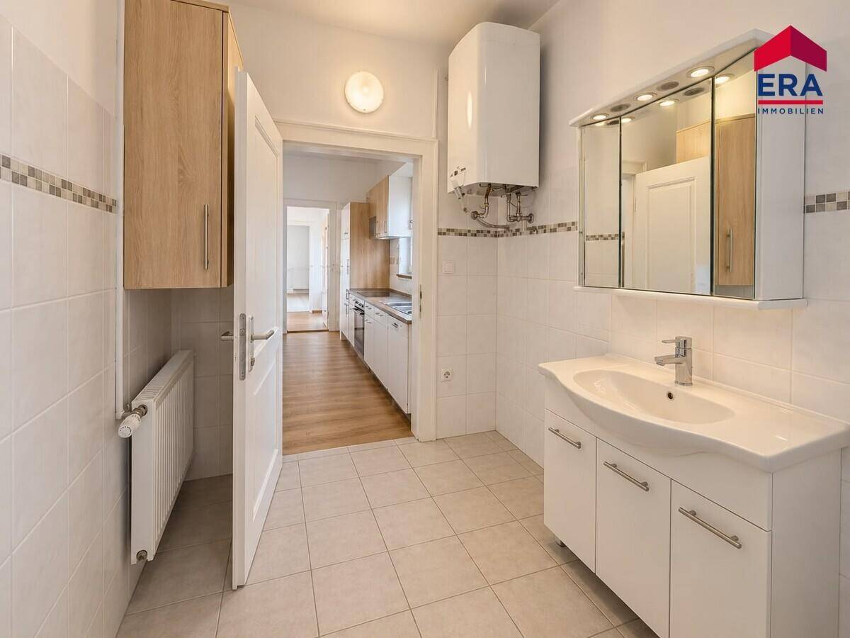Modernes Badezimmer mit Waschtisch, Spiegelschrank und Fliesenboden, bietet direkten Zugang zur Küche.