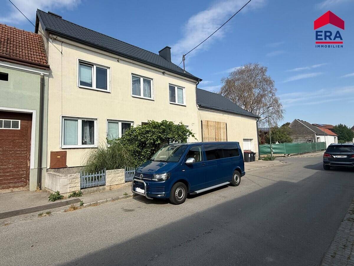 Ansicht des Wohnhauses von der Straße mit einem geparkten blauen Van und dem ERA-Logo.