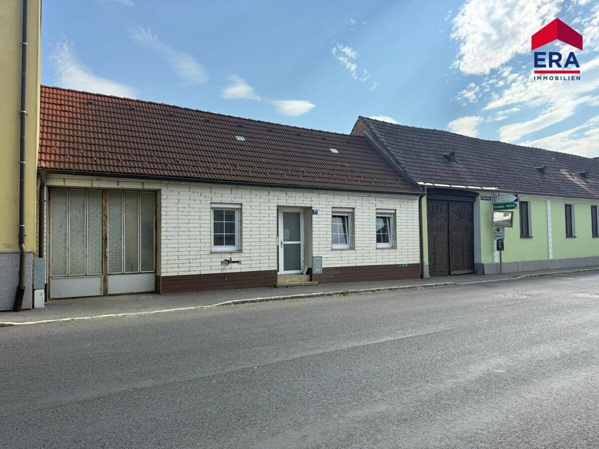 Breitere Ansicht des Hauses mit angrenzendem Gebäude und Straße unter blauem Himmel.