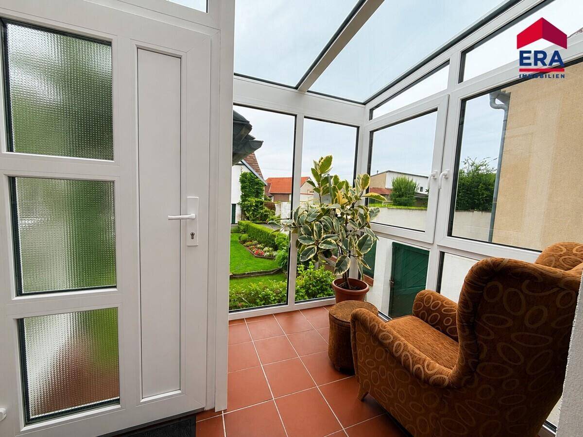 Heller Wintergarten mit Glaswänden, Terrakottafliesen und einem Sessel, bietet einen schönen Blick in den Garten.