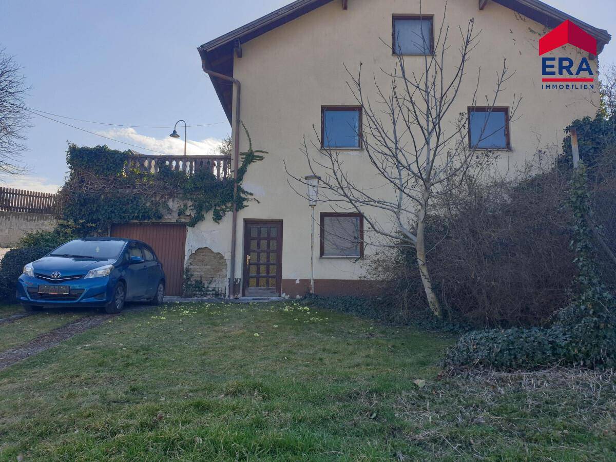 Ansicht des Hauses von außen mit einem Auto davor und einem Gartenbereich.