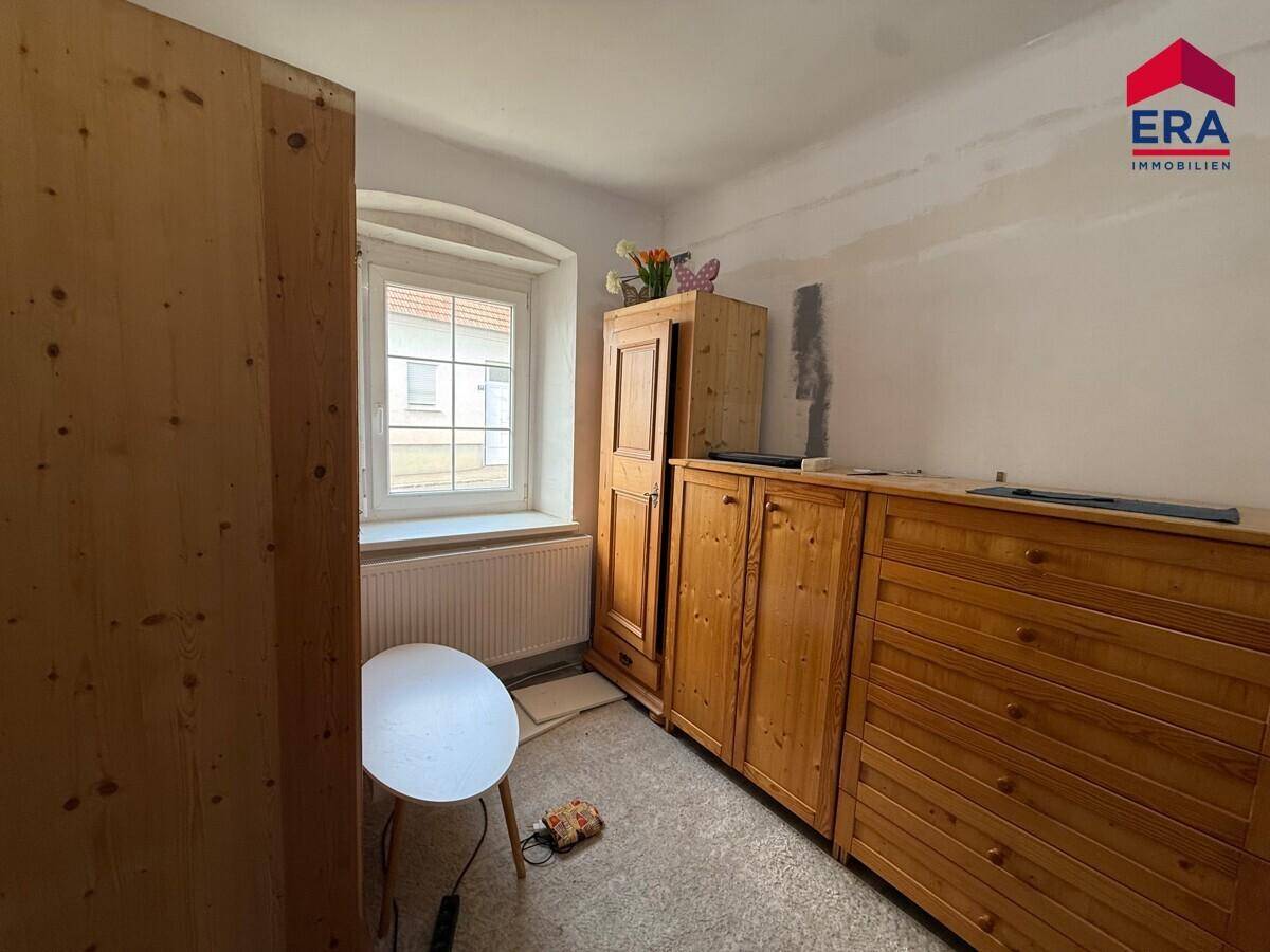 Kleines Schlafzimmer mit Holzmöbeln, einem Fenster und hellem Bodenbelag, bereit zur Renovierung.
