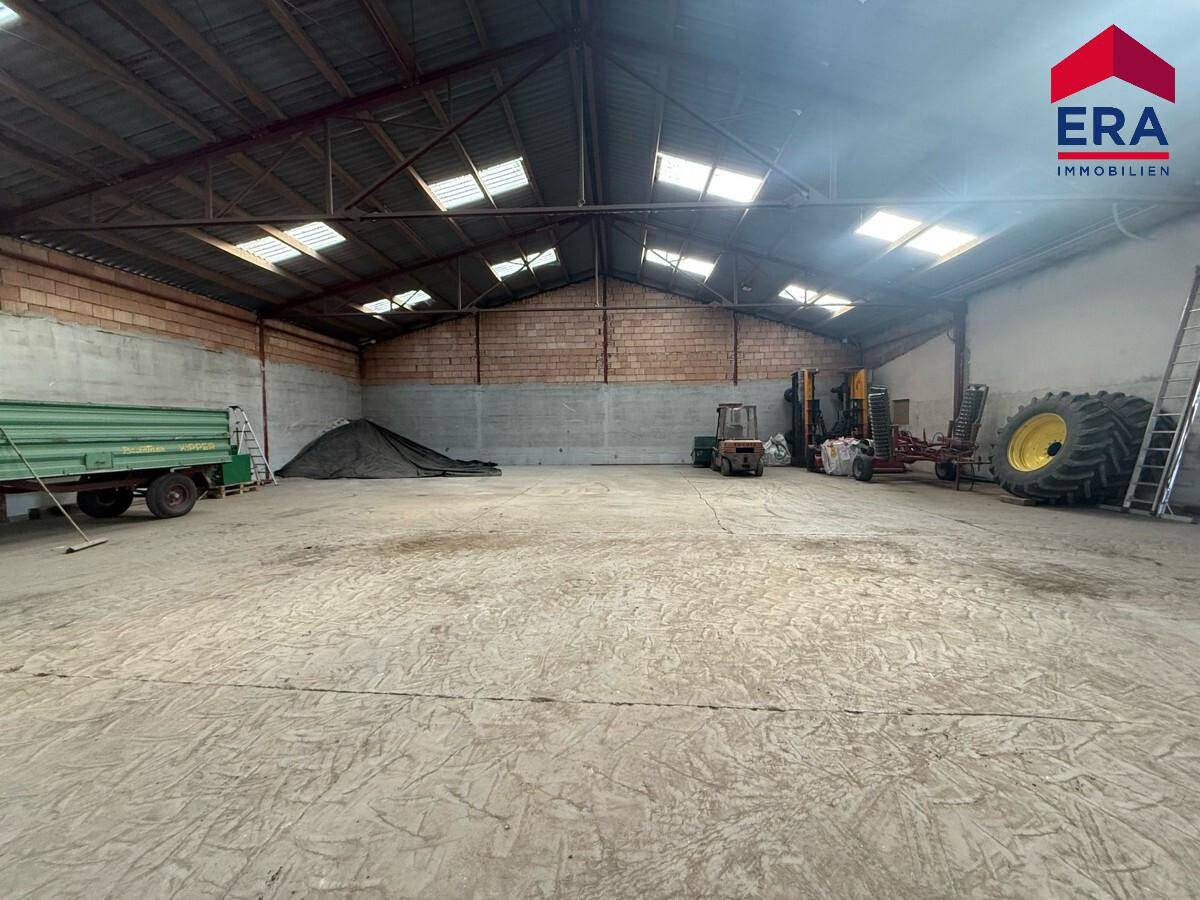 Große, offene Lagerhalle mit Betonboden und sichtbarer Dachkonstruktion, ideal für Maschinen und Material.