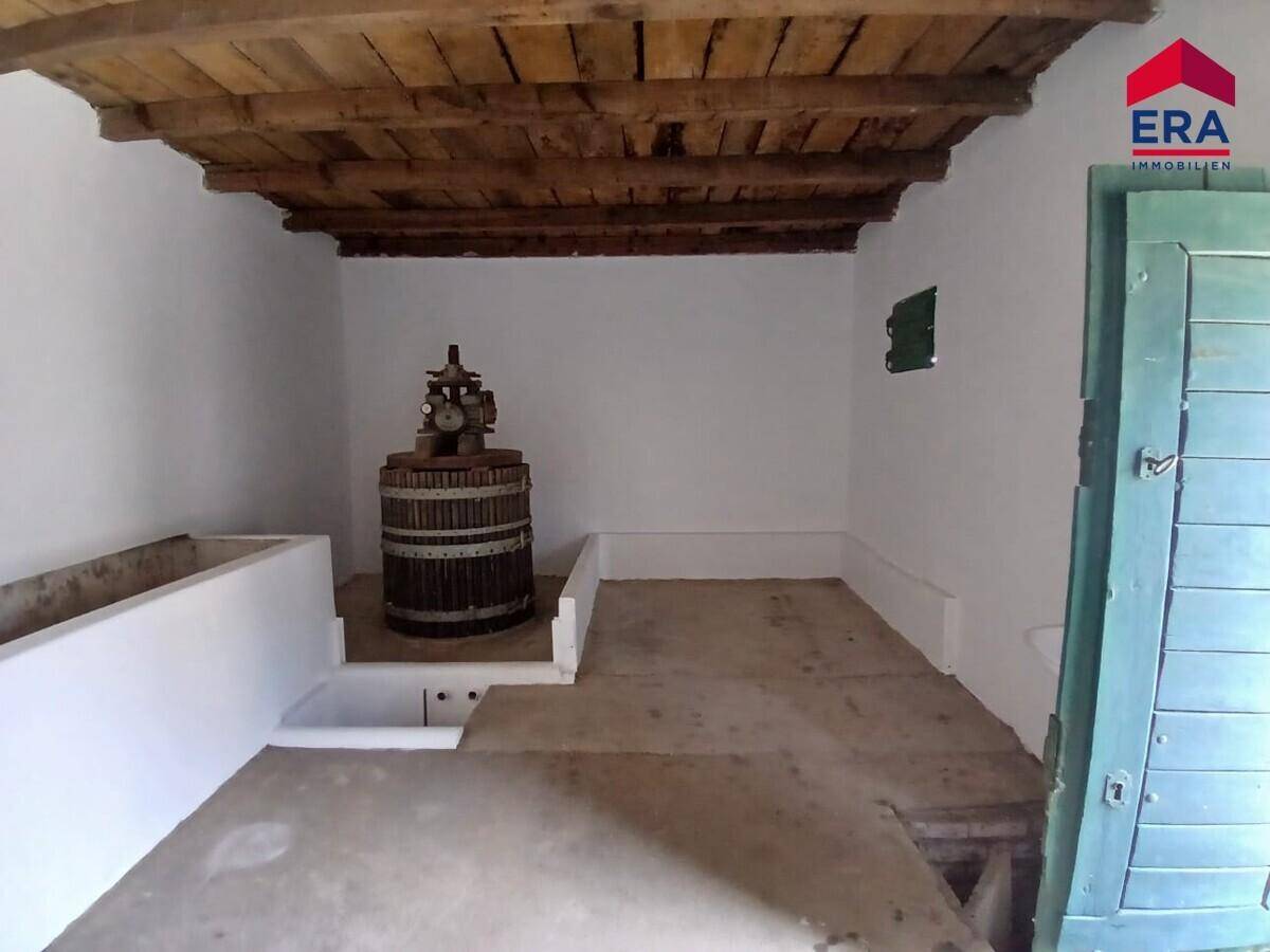 Innenansicht eines Raumes mit sichtbaren Holzbalken, alter Weinpresse und einfachen Oberflächen.