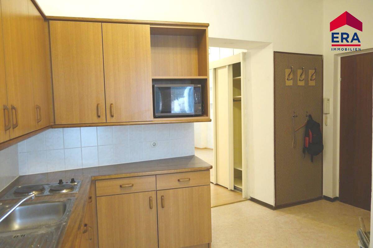 Kleine Küchenzeile mit Holzschränken, Kochfeld und Mikrowelle, ideal für kleine Wohnungen.