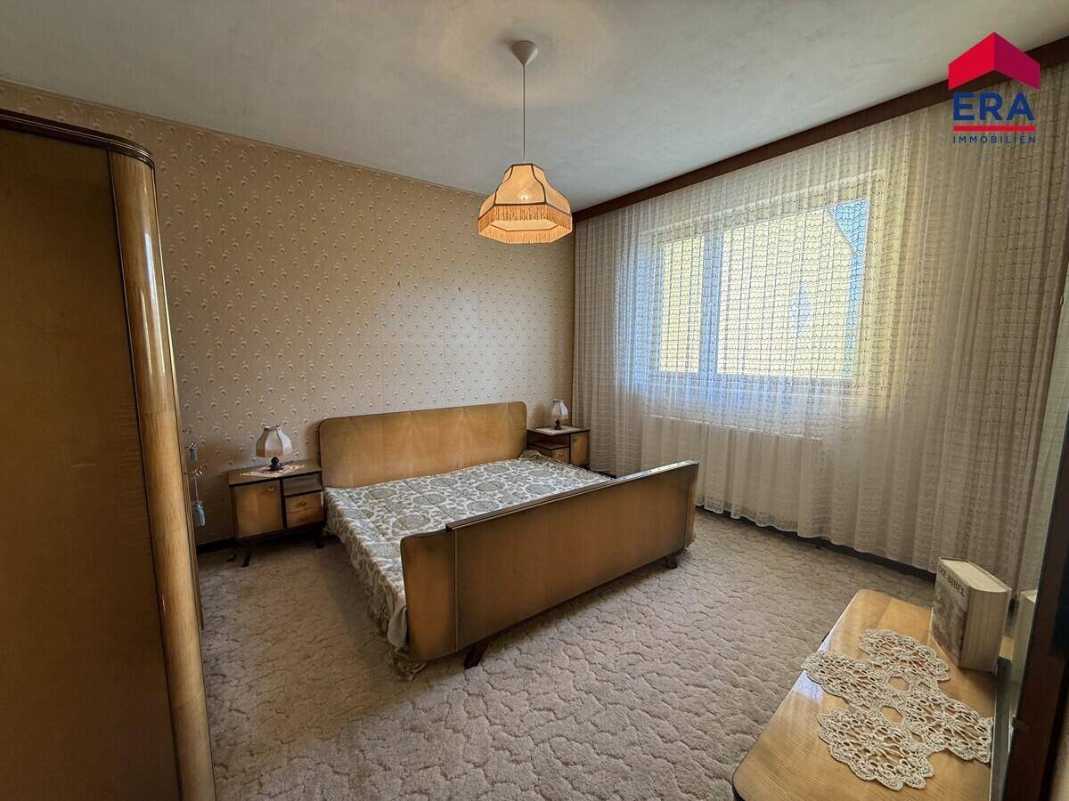 Schlafzimmer mit Teppichboden, Doppelbett und gemusterter Tapete, im traditionellen Stil.