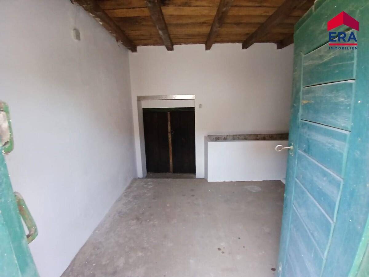 Einfacher Innenraum mit Betonboden und Holzbalkendecke, ideal als Lager- oder Arbeitsbereich.