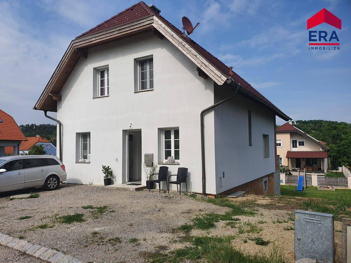 Vorderansicht des Einfamilienhauses mit Kiesauffahrt und Satteldach unter blauem Himmel.