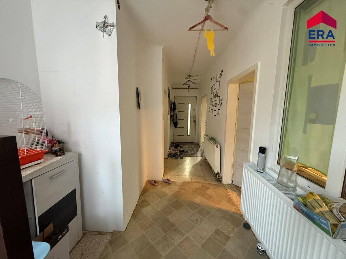 Heller Flur mit Fliesenboden, Heizkörper und Fenster, der den Eingangsbereich verbindet.