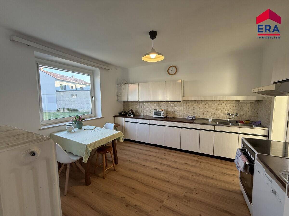 Funktionale Küche mit Essbereich, weißen Schränken und einem Fenster mit Blick ins Grüne.