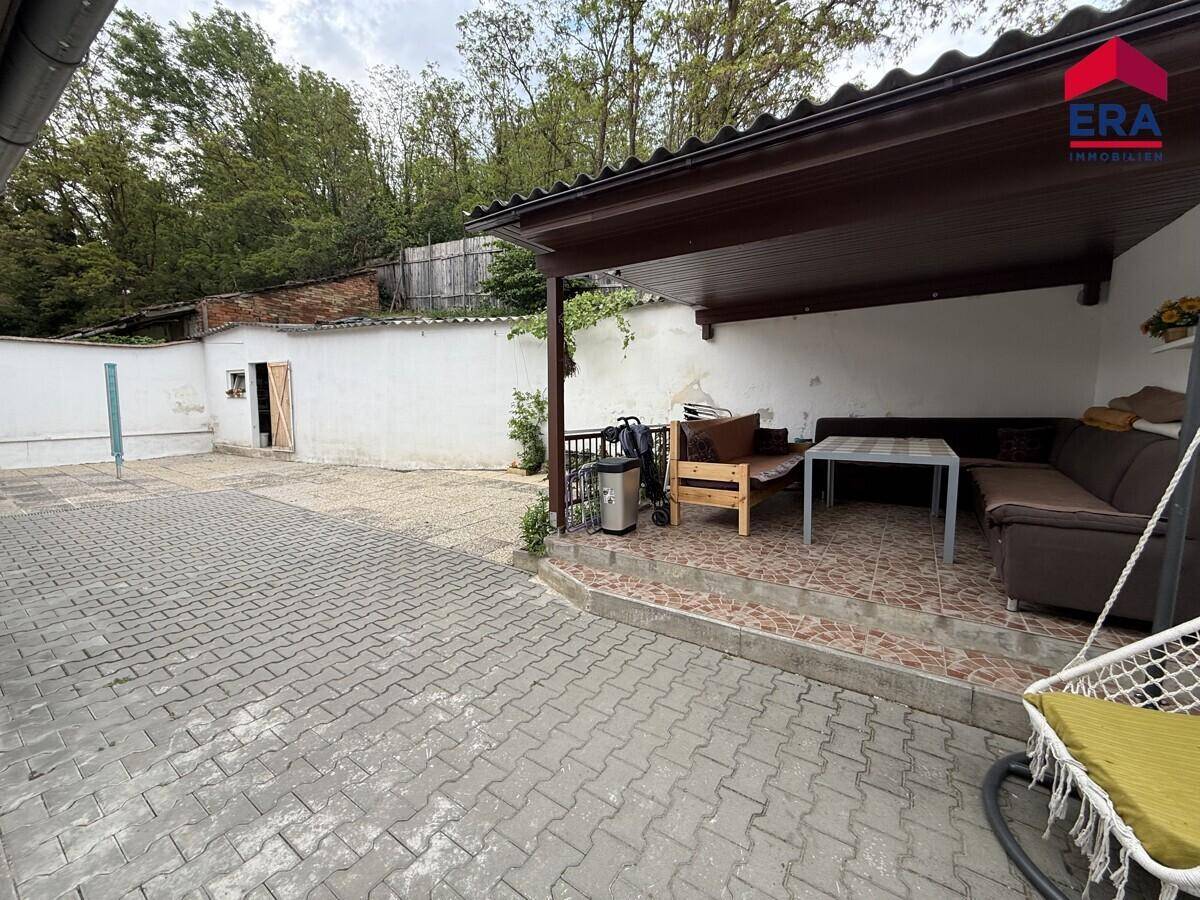 Gepflasterter Außenbereich mit überdachter Terrasse, Sitzgelegenheiten und Schaukelstuhl.