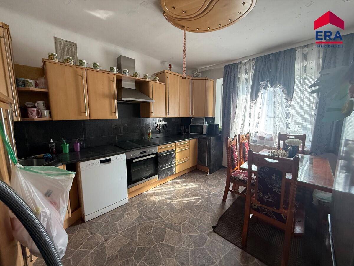 Geräumige Wohnküche mit Essbereich, Holzschränken und Blick auf den Vorhang.