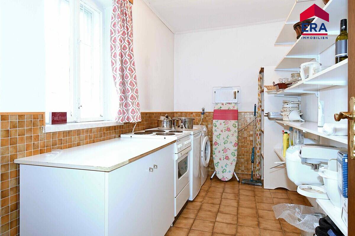 Praktischer Hauswirtschaftsraum mit einfacher Küchenzeile, Waschmaschine und Regalen.