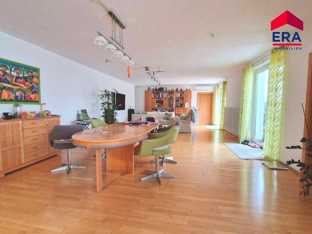 Geräumiger offener Wohn- und Essbereich mit hellem Parkettboden und Zugang zum Balkon.