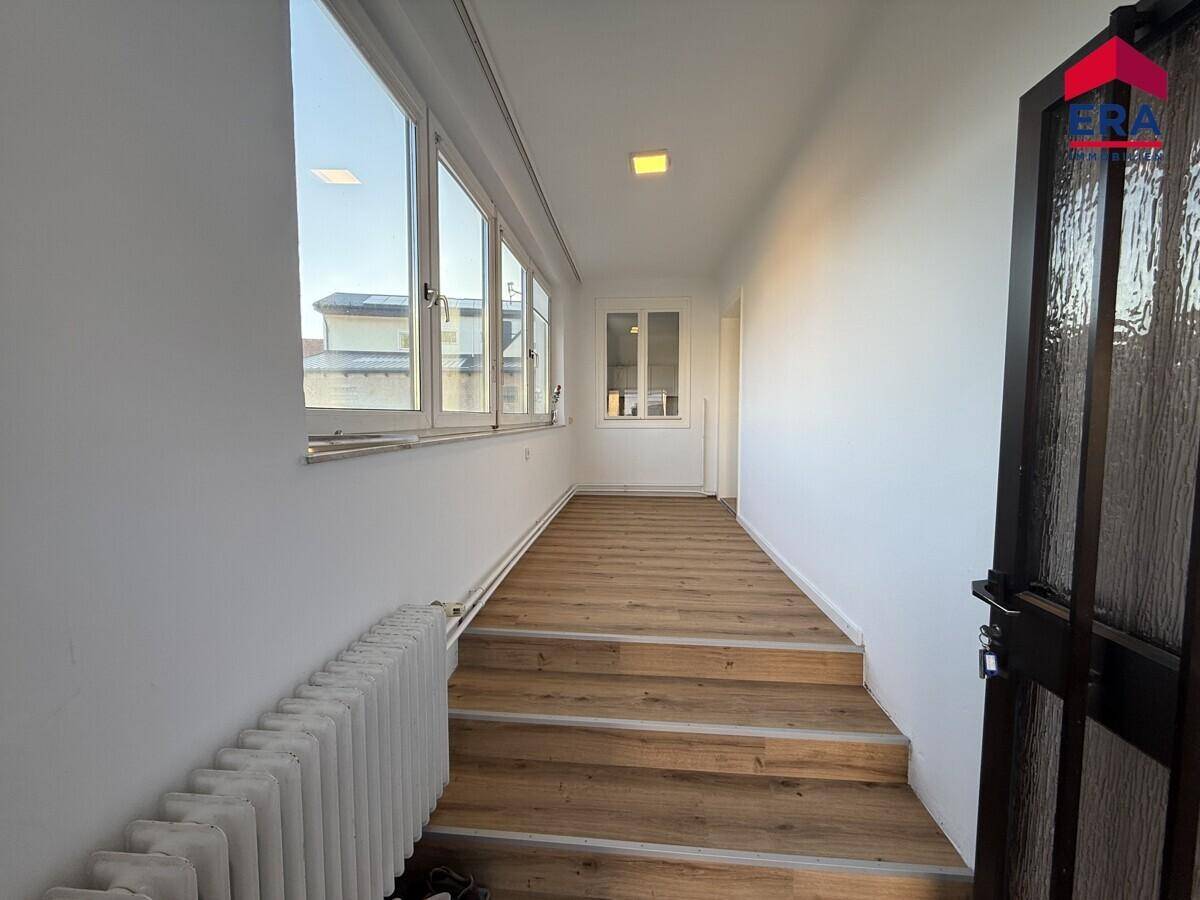 Heller Flur mit Holztreppe, großen Fenstern und einem klassischen Heizkörper.