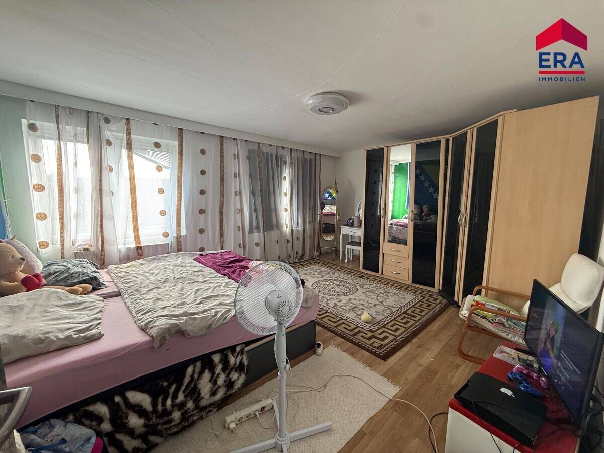 Kinderzimmer mit Bett, Kleiderschrank und Fenster, das viel Tageslicht hereinlässt.