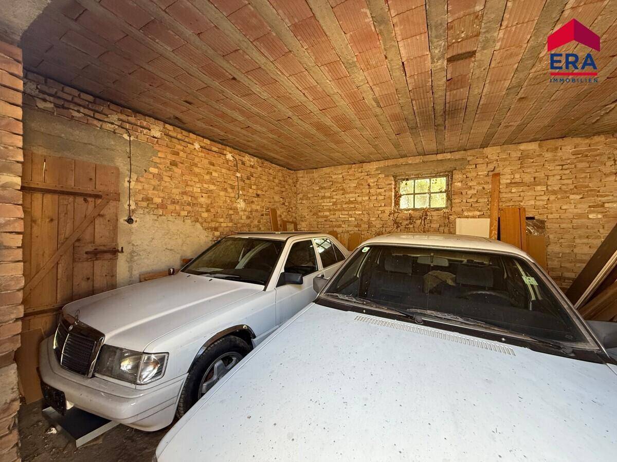 Geräumige Garage mit zwei Autos, unverputzten Backsteinwänden und einer Holzdeckenkonstruktion.