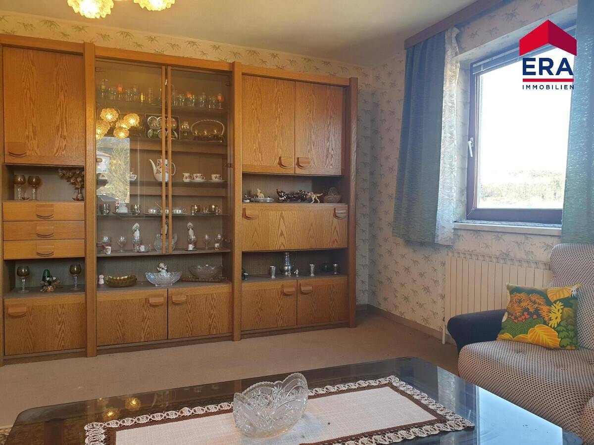 Wohnzimmer mit traditionellen Holzschränken, gemusterter Tapete und Blick ins Grüne.