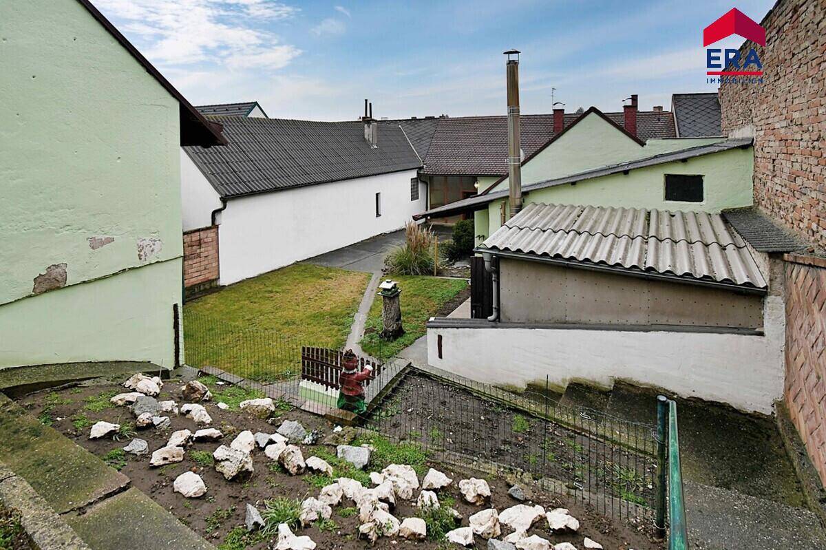 Blick auf den Gartenbereich mit Rasen, Steinen und angrenzenden Gebäuden.