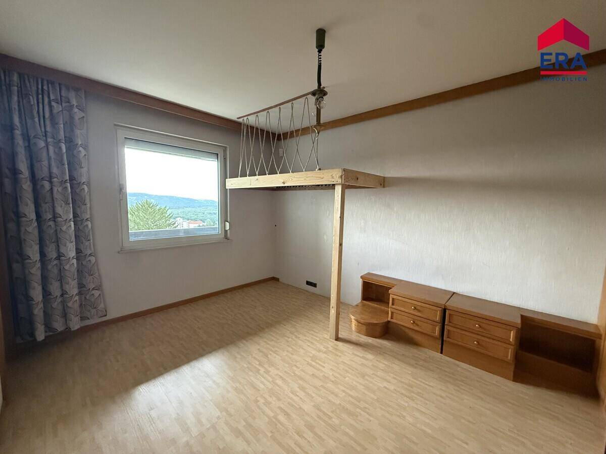 Helles Schlafzimmer mit Laminatboden, großem Fenster und einer erhöhten Schlafebene.