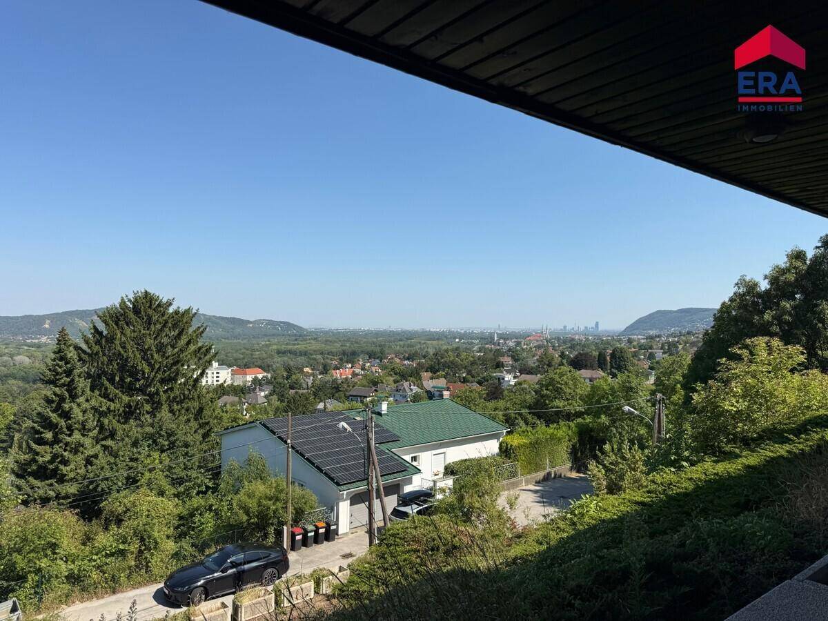 Weitläufiger Panoramablick über das Tal mit Häusern, Bäumen und einer fernen Stadtkulisse.