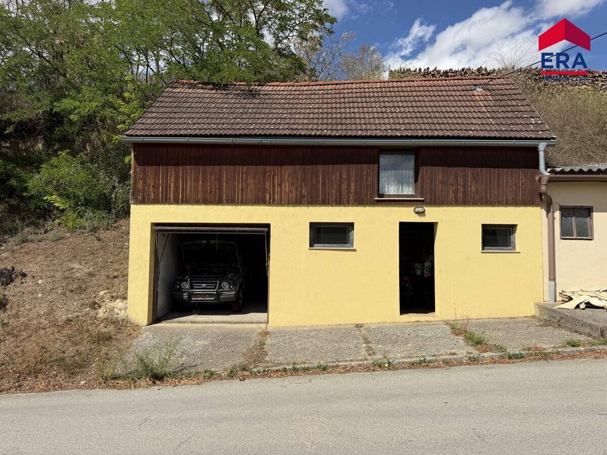 Gebäude mit integrierter Garage im Erdgeschoss und einer Holzfassade im oberen Bereich unter einem Ziegeldach.