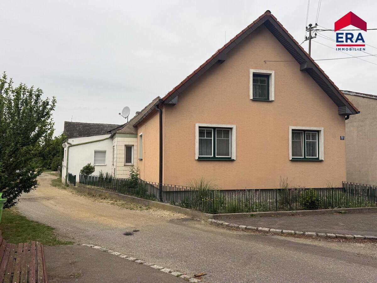 Ansicht eines Einfamilienhauses mit pfirsichfarbener Fassade, roten Dachziegeln und grünen Fensterrahmen von der Straße aus.