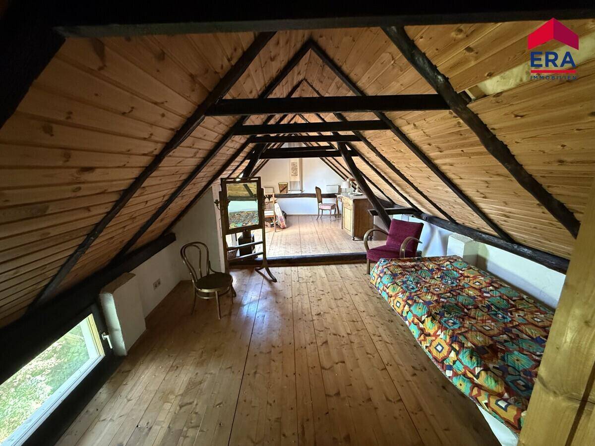 Ausgebauter Dachboden mit schrägen Holzdecken, sichtbaren Balken und einem Schlafbereich.