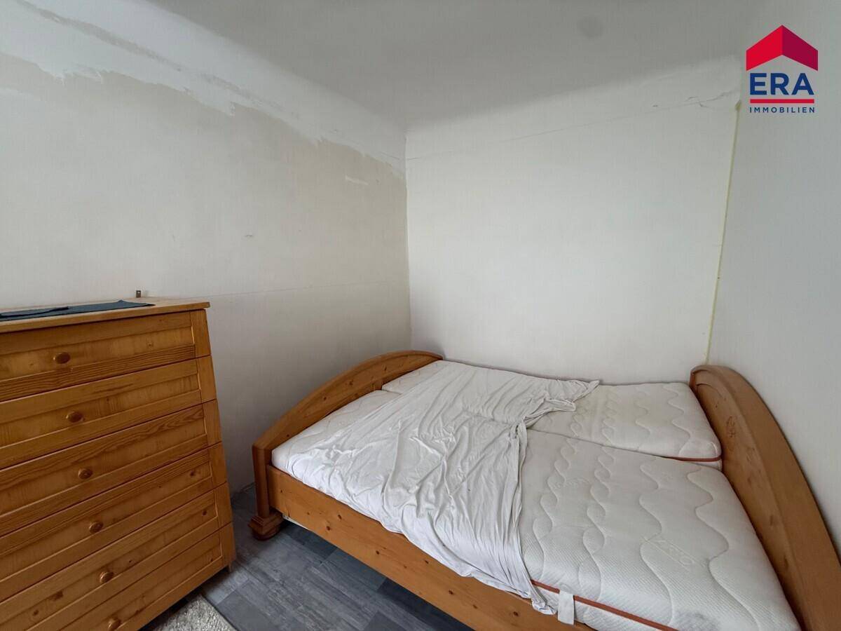 Schlafzimmer mit Holzbettrahmen, Kommode und modernem dunklem Laminatboden, hell gestrichene Wände.