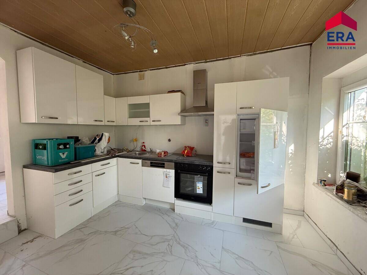 Moderne Einbauküche mit weißen Hochglanzfronten und Fliesenboden, derzeit in Renovierung.