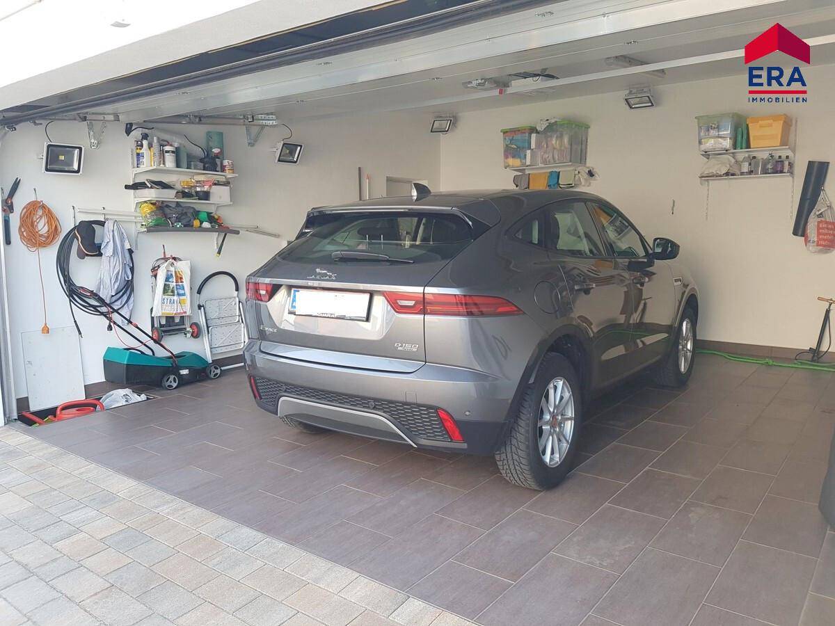 Garage mit einem geparkten Auto, Fliesenboden und Regalen für Werkzeuge und Lagerung.