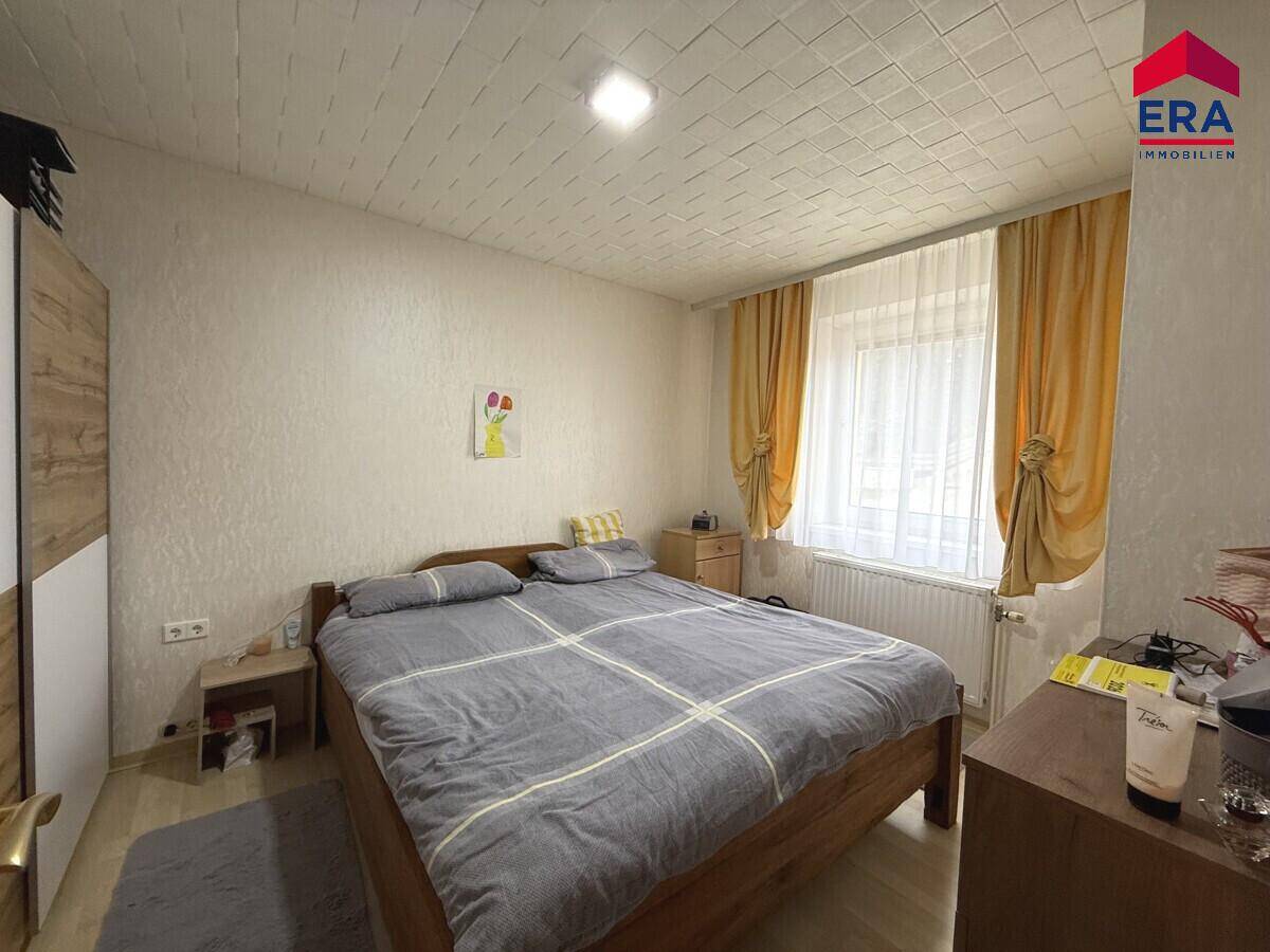 Helles Schlafzimmer mit Doppelbett, Nachttischen und Vorhängen am Fenster.