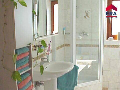 Helles Badezimmer mit Duschkabine, Waschbecken und Spiegelschrank, gefliest.