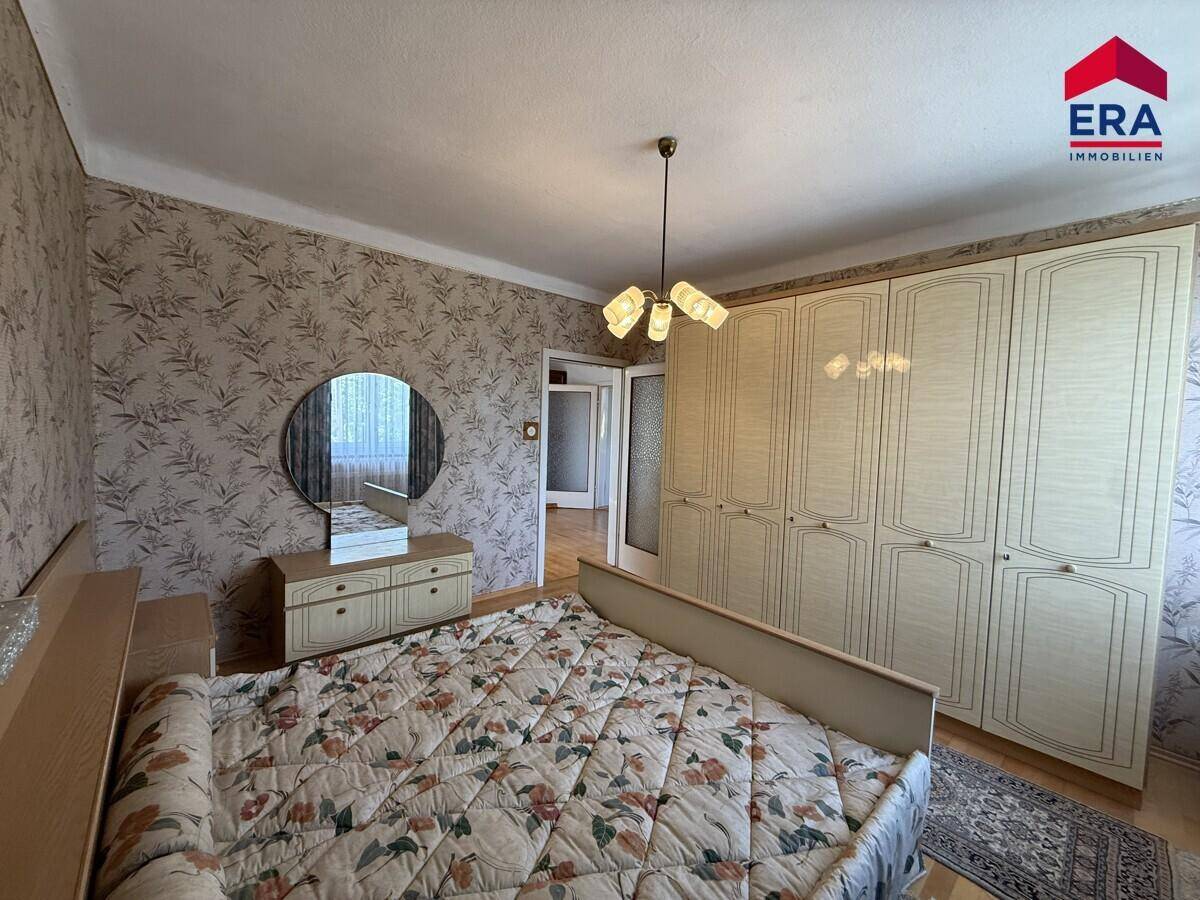 Schlafzimmer mit Doppelbett, großem Kleiderschrank und gemusterter Tapete.