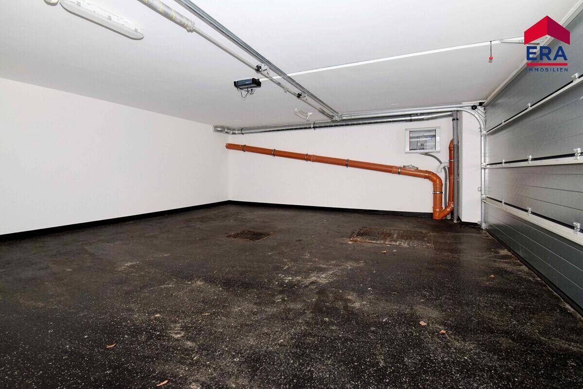 Geräumige Garage mit Betonboden, sichtbaren Rohren und Rolltor.