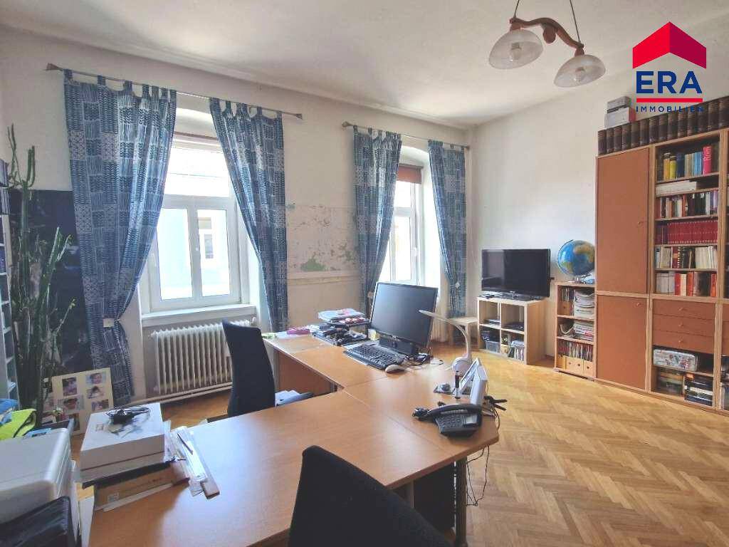 Arbeitszimmer mit Fischgrätparkett, großem Schreibtisch und Bücherregalen an den Wänden.