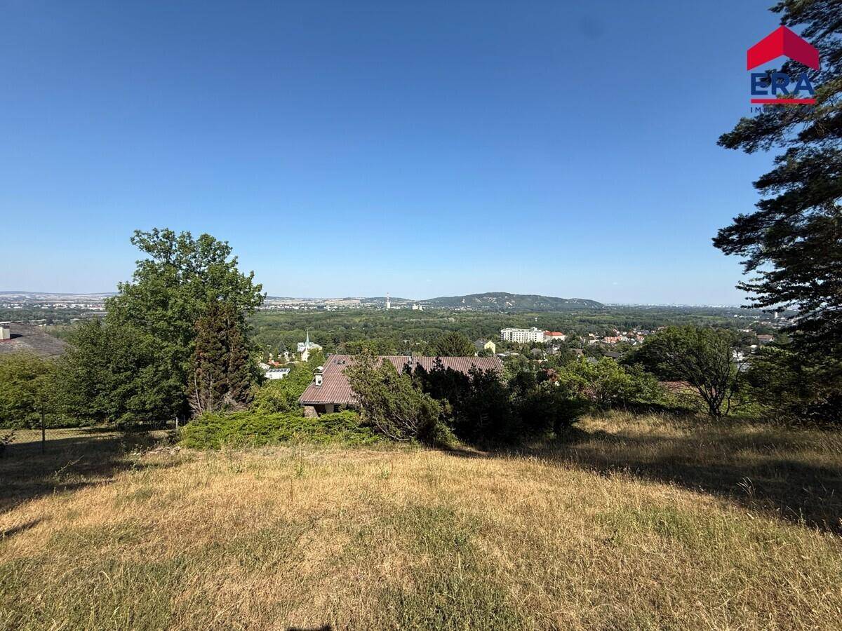Weitläufiger Panoramablick über grüne Hügel und eine entfernte Stadtlandschaft unter blauem Himmel.