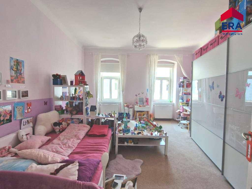 Kinderzimmer mit rosa Wänden, Teppichboden und vielen Spielsachen und Dekorationen.
