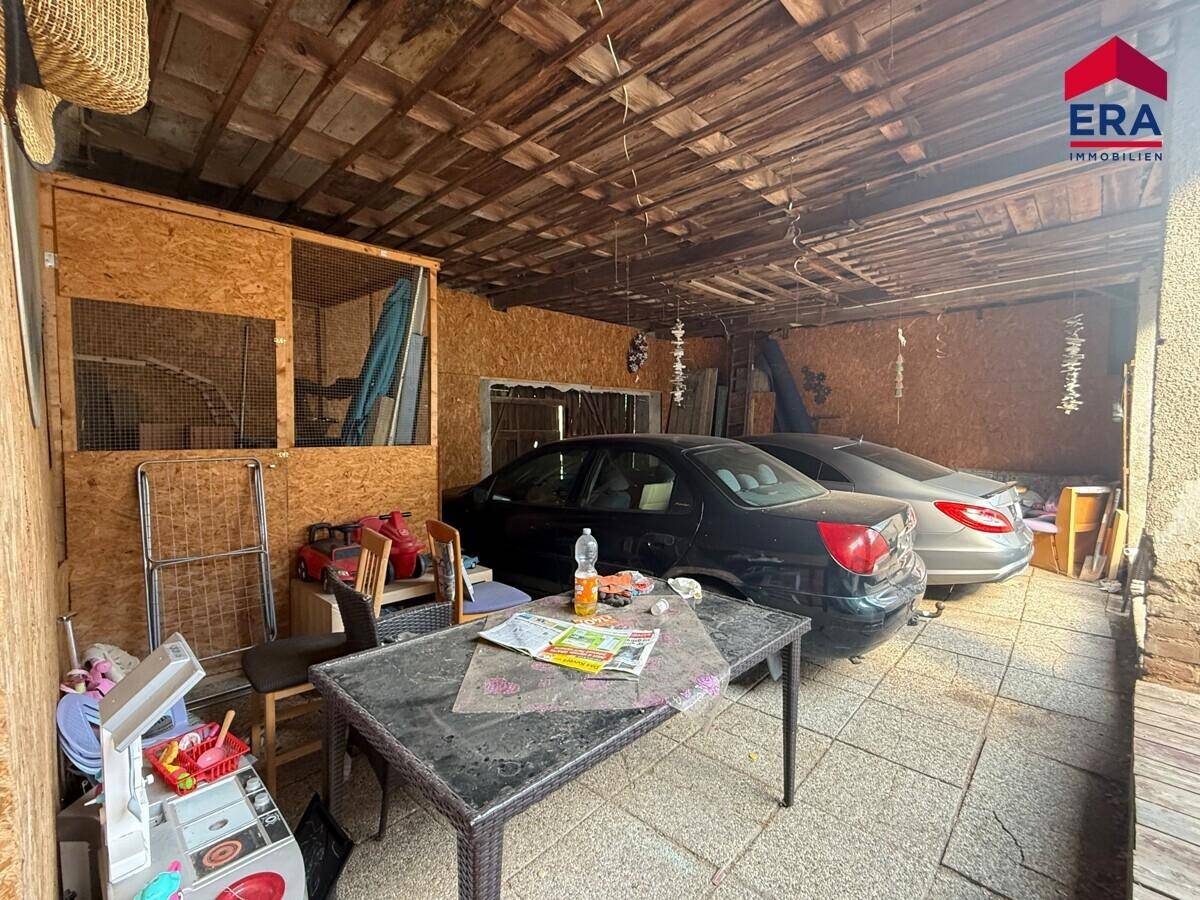 Überdachter Garagenbereich mit zwei geparkten Autos und Lagerflächen.