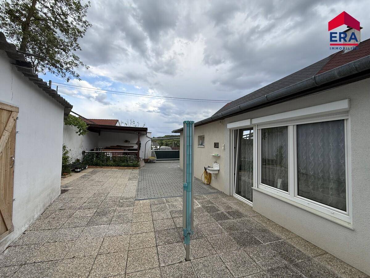 Gepflasterter Außenbereich neben dem Haus mit Fenster und Außenwaschbecken.