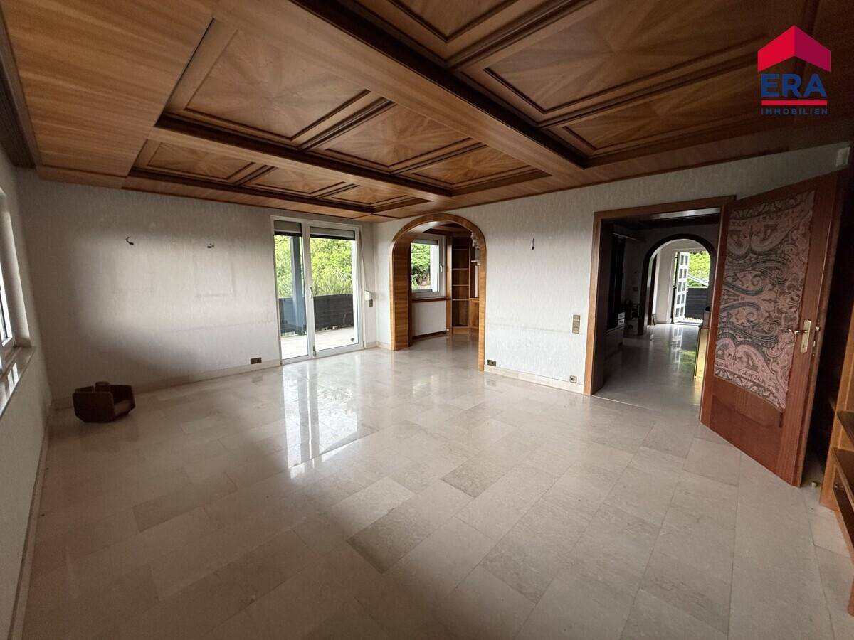 Geräumiges Wohnzimmer mit heller Steinfliesenboden, aufwendiger Holzdecke und Zugang zum Balkon.