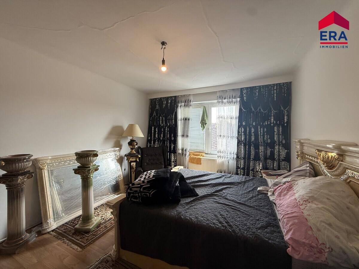 Schlafzimmer mit großem Bett, Nachttischen und Fenster mit dunklen Vorhängen.