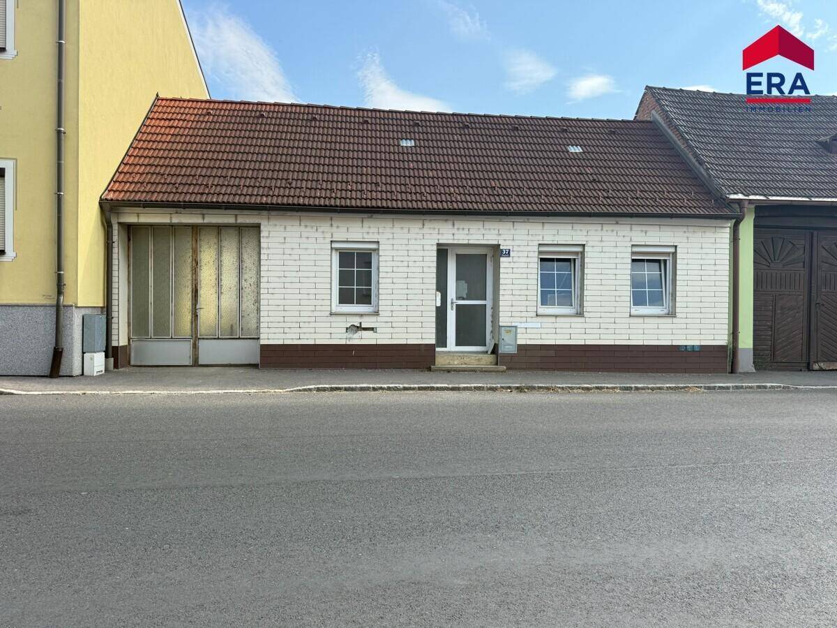 Vorderansicht eines kleinen Hauses mit weißer Ziegelfassade, rotem Ziegeldach und Garagentor.