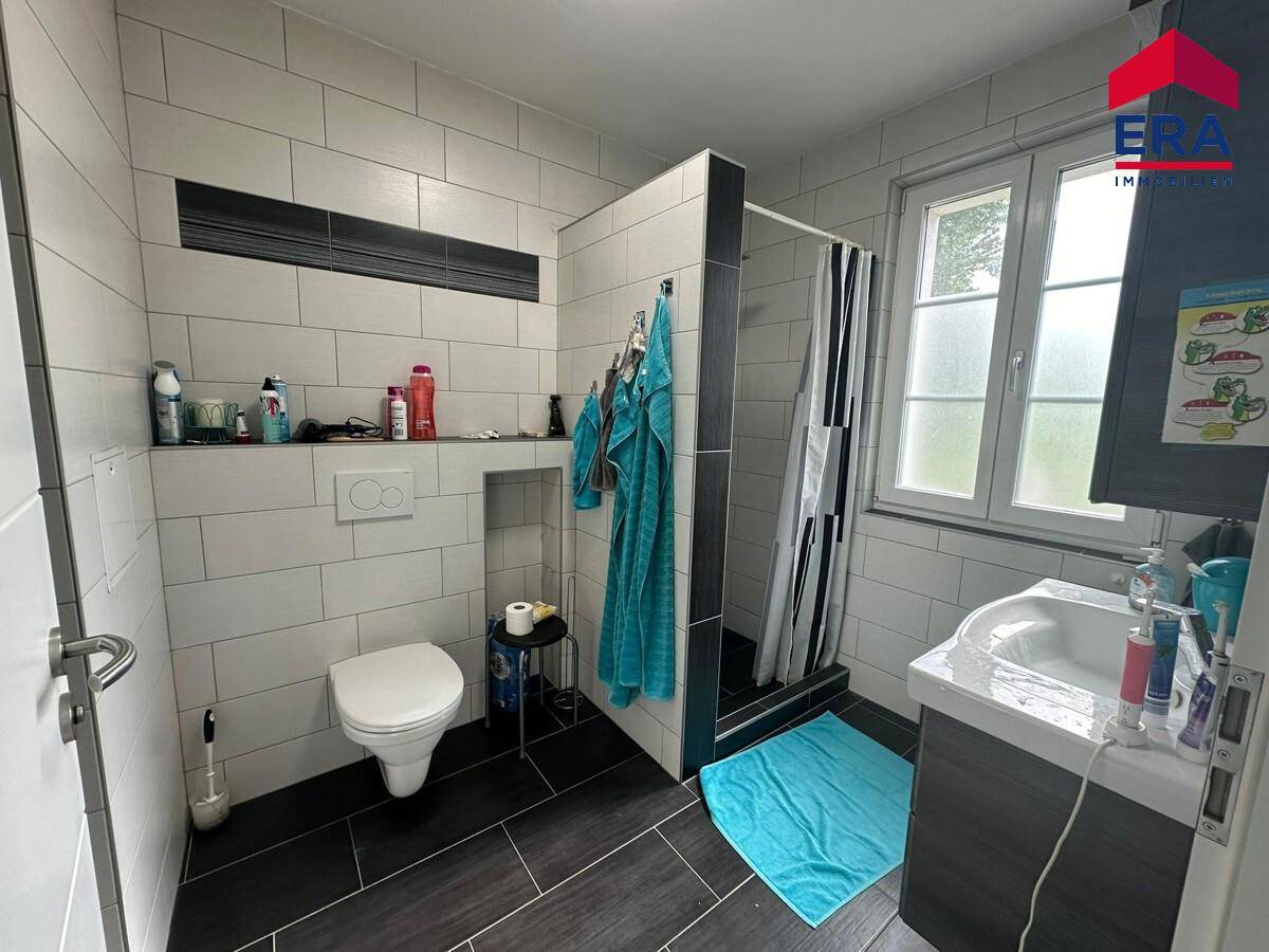 Modern gefliestes Badezimmer mit Dusche, WC und Fenster für Tageslicht.