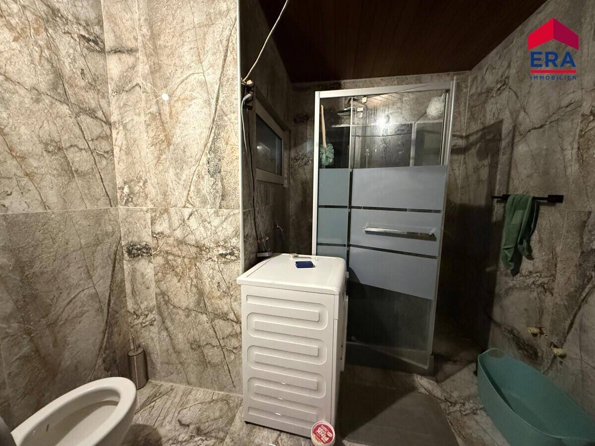 Badezimmer mit gemusterten Fliesen, Duschkabine, Toilette und Waschmaschine, funktional eingerichtet.