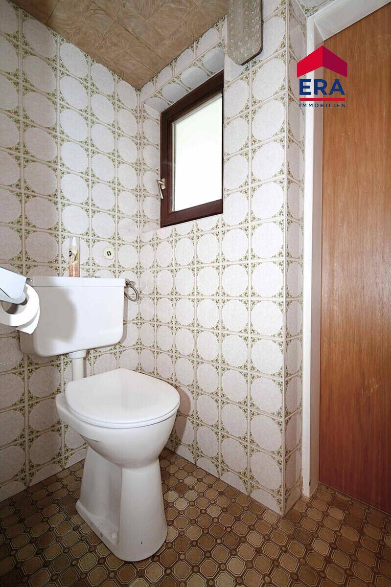 Separate Toilette mit Fenster und gemusterten Fliesen.