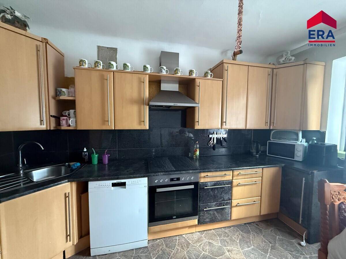 Funktionale Küche mit Holzschränken, dunkler Arbeitsplatte und integrierten Geräten.
