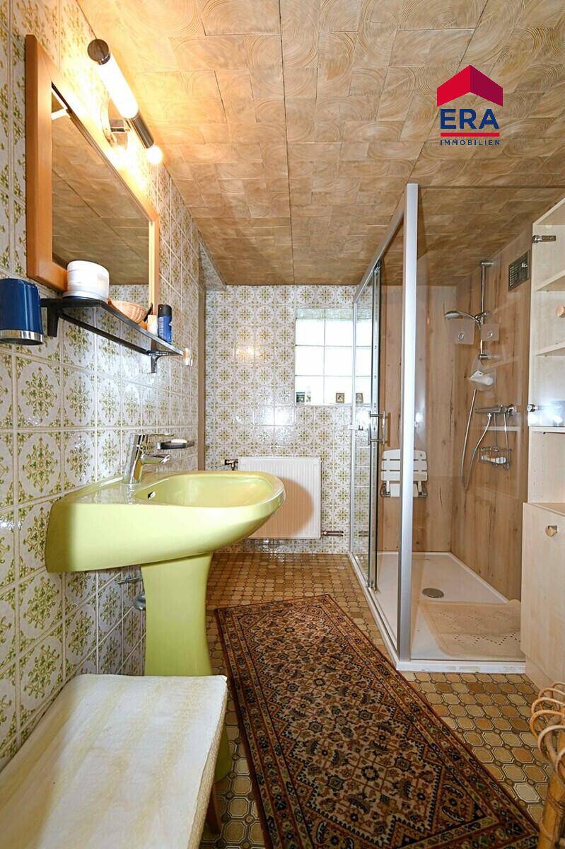 Badezimmer im 80er-Jahre-Stil mit Duschkabine, gelbem Waschbecken und gemusterten Fliesen.